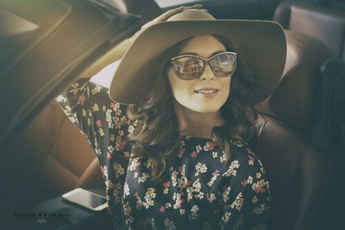 Lächelnde Frau mit breitkrempigem Sonnenhut, Sonnenbrille und geblümtem Kleid sitzt im Auto – sommerliche Peoplefotografie in Gera